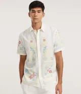 Camisa de lino y algodón color blanco con cuello inglés, manga corta y cierre frontal de botones. Presenta un diseño de bordado fino floral y de aves de estilo artesanal.