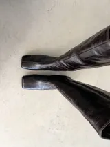 Bota alta de caña recta confeccionada en cuero con efecto arrugado color marrón oscuro, de punta cuadrada y tacón ancho.