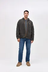 Campera de sherpa con diseño capitoneado en color crema. Presenta cierre frontal completo, cuello alto, bolsillos laterales y un bolsillo en el pecho con cierre en contraste. Incluye detalles en nylon y bordado decorativo en el pecho.