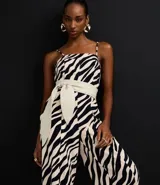 Mono largo de sastrería marca Cortelle, confeccionado en crepé con elastano, con estampado animal print de cebra en tonos beige y negro. Presenta escote recto, tirantes finos regulables, corte wide leg en las piernas y un cinturón ancho ajustable en la cintura.