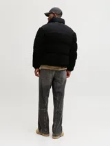 Campera puffer con cuello alto y cierre frontal, confeccionada en tejido teddy negro con paneles superiores lisos. Cuenta con bolsillos laterales y relleno de poliéster.