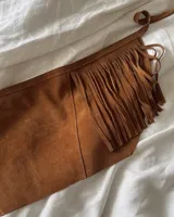 Culerito de descarne vacuno color negro, con diseño envolvente y flecos laterales. Cuenta con tiras para atar en la cintura y etiqueta de la marca Lucy in the Sky.