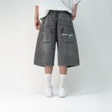 Bermuda de jean estilo baggy en color negro lavado, con corte holgado y largo por debajo de la rodilla. Presenta bolsillos traseros amplios con un bordado en hilo blanco.