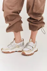 Championes de estilo urbano en color blanco con detalles en tono arena. Presentan un diseño con doble tira de velcro en el empeine, suela de plataforma dentada en color caramelo y tirador en el talón.