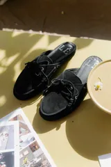 Mocasines tipo mule de gamuza negra con cordones decorativos.