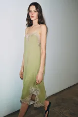 Vestido midi de satén color verde oliva, con escote recto y tirantes finos ajustables. Presenta detalles de encaje en color crema en el escote y en el bajo, con aberturas laterales.