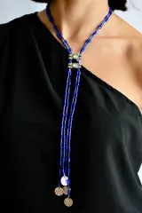 Collar largo de cuentas tubulares color azul eléctrico, con piezas centrales metálicas decoradas con cristales y terminaciones con dijes circulares texturizados en tono plateado.