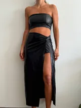 Pollera midi negra de cuero sintético, con tajo lateral y detalle drapeado en la cintura.