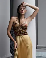 Vestido con falda plisada color dorado y top diseñado en jacquard con estampado paisley en tonos borgoña, ocre y dorado. Se ajusta al cuello con tiras de cadenas doradas.