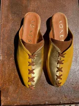 Zapatos tipo mule de punta cerrada y talón abierto, con diseño bicolor en tonos dorado y mostaza, con detalles cruzados en el empeine y suela baja.