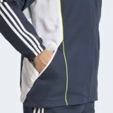 Campera deportiva Adidas de entrenamiento del Real Madrid, color azul marino con paneles laterales blancos y ribetes finos en amarillo neón. Presenta cierre frontal, cuello alto y el escudo del club bordado en el pecho.