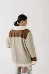 Gamulán de paño en color beige jaspeado con detalles en cuero sintético marrón y forro de corderito sintético blanco. Presenta cierre frontal cruzado, cuello solapa, bolsillos laterales y puños con vuelta.