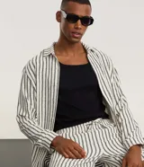 Camisa de manga larga con cuello inglés y cierre frontal de botones. Presenta un diseño de rayas verticales en tonos neutros, confeccionada en tejido de poliéster con caída estructurada y corte comfort.
