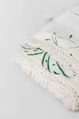 Pareo de playa blanco con estampado de hojas verdes y borde de encaje con flecos.