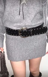 Cinto de cuero sintético negro con tachas metálicas circulares en todo su largo y hebilla metálica plateada de diseño redondeado.