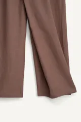 Pantalón de corte relajado confeccionado en tejido fluido con mezcla de viscosa y lino. Presenta un diseño cruzado en la cintura con cierre de cremallera, botón y trabilla ajustable. Cuenta con bolsillos laterales y bolsillos traseros de vivo con botón.