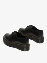 Zapato de cuero negro con plataforma gruesa y costuras amarillas. Tiene cordones negros y una puntera ancha y redondeada.