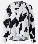 Blusa de crepé color blanco con estampado abstracto en negro, cuello redondo con cordón ajustable, mangas largas y barra trasera alargada.