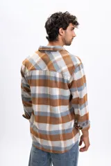 Sobrecamisa de manga larga con diseño a cuadros en tonos tostado, gris y blanco. Presenta cuello clásico, cierre frontal con botones y dos bolsillos delanteros con solapa.