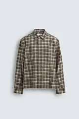 Camisa de corte relajado con estampado de cuadros en tonos marrones y blancos. Presenta cuello clásico, cierre frontal de botones, manga larga con puños abotonados y un bolsillo plastrón en el pecho.