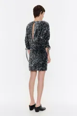 Vestido corto negro con lentejuelas plateadas, mangas abullonadas 3/4 con lazos ajustables y corte recto.