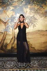 Vestido largo negro de encaje con escote profundo halter, espalda abierta, detalles fruncidos al cuerpo y falda larga semitransparente con tiras largas para atar.