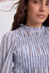 Blusa celeste a rayas marrones y blancas, con diseño de punto smock en el pecho y mangas largas abullonadas con puños elásticos.