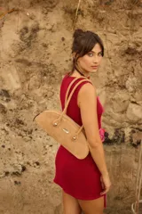 Cartera estilo baguette de cuero, con diseño alargado y estructurado. Presenta manijas largas con detalles de nudos esféricos metálicos en la unión y cierre superior.