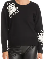 Buzo tejido color negro con cuello a la base y mangas largas. Presenta un diseño floral en relieve en color blanco ubicado en la parte superior delantera y en la parte inferior de una de las mangas.