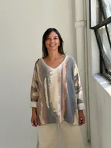 Sweater de punto con diseño abstracto de rayas verticales en tonos gris, beige y terracota. Presenta cuello en V, corte holgado y mangas largas con puños vueltos.