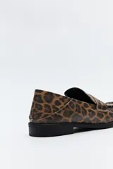 Mocasín de cuero sintético negro con punta cuadrada, detalle de costuras visibles en la capellada y taco bajo.