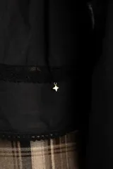Blusa negra de algodón con diseño de broderie y calados en el pecho y hombros. Presenta corte oversize, mangas largas con puños y un detalle de volado en la cintura.