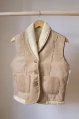 Chaleco de cuero genuino con interior de piel sintética, diseño con cuello solapa, cierre frontal de tres botones y dos bolsillos delanteros aplicados.