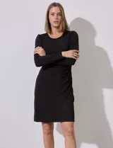 Vestido corto negro de seda fría con escote redondo y mangas largas abullonadas. Presenta frunces laterales que estilizan la figura.