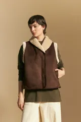 Chaleco negro de gamuza sintética con interior y bordes de corderito sintético. Presenta un diseño sin mangas con cuello solapa y cierre frontal.