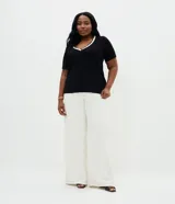Blusa de viscolycra color beige con escote en V y cuello doble en tono negro con borde de ondas, de mangas cortas y corte amplio.