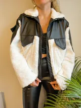 Campera con cierre frontal, de cuero sintético negro y corderito blanco, con cuello solapa y bolsillos plaqué.