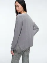 Sweater de punto gris con escote en V profundo, hombros caídos y mangas largas. Presenta un diseño de calce relajado con sutiles micro lentejuelas integradas en el tejido.