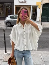 Camisa oversize blanca con botones frontales de madera, cuello clásico y mangas amplias con detalles de volados.