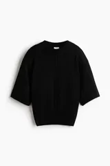 Top de punto negro con costura central delantera, mangas cortas con hombros caídos y ribete acanalado en cuello, puños y bajo.