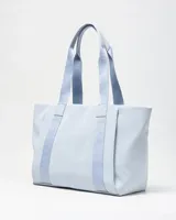 Cartera tipo tote color celeste, con asas de hombro y tiras frontales con la inscripción de la marca en relieve. Cuenta con un pequeño aplique circular con el logo en el centro.