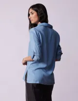 Blusa de lyocell color azul claro, con cuello camisero, escote en V con tapeta de botones y mangas largas con presilla para regular el largo.