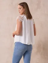 Blusa negra de crepe con apliques de crochet en los hombros. Tiene cuello redondo, mangas cortas y espalda con abertura ojal y botones.