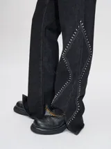 Pantalón de jean tiro alto con corte ochentoso y terminación oxford. Presenta apliques metálicos decorativos alrededor de los bolsillos delanteros y traseros, y a lo largo de la parte externa de las piernas.