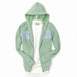 Campera con capucha verde agua y detalle de franja horizontal lila en la parte superior del pecho. Cierre frontal con cremallera y bolsillos tipo canguro.