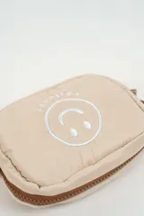 Neceser acolchado color beige con diseño de carita feliz bordada en el frente y cierre superior con tirador de cordón.