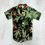 Camisa de manga corta con estampado de hojas y flores rojas y amarillas sobre fondo negro.