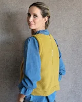 Chaleco de tela bucle color tostado, con diseño sin mangas, cuello redondo y corte recto. Presenta costuras verticales decorativas en el frente.