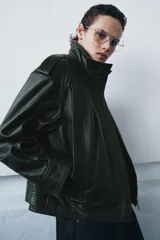 Chaqueta bomber de piel color verde oscuro, con cuello alto, manga larga con puño, bolsillos delanteros y trabillas en los hombros. Cierre frontal con cremallera y botones ocultos por solapa.