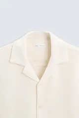 Camisa de corte regular fit confeccionada en tejido con estructura de color negro. Cuenta con cuello bowling, manga corta, aberturas laterales en el bajo y cierre frontal de botones.